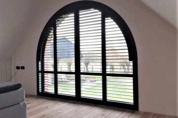 Halfrond raam met zwarte shutters in slaapkamer