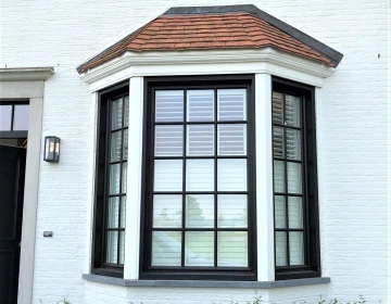 Zwarte shutters in witte woning met erker